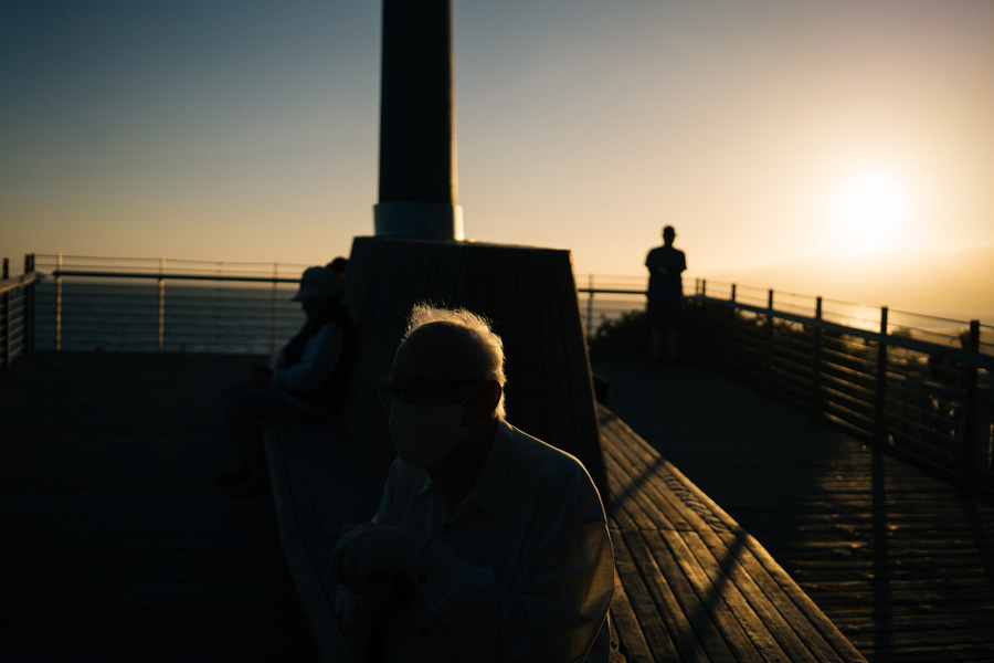 A senior man sitting on a bench by the ocean.