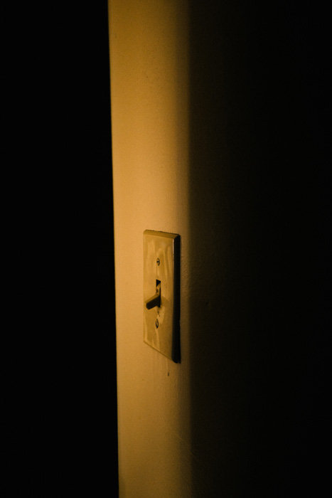 A wall light switch in a dim shaft of light.