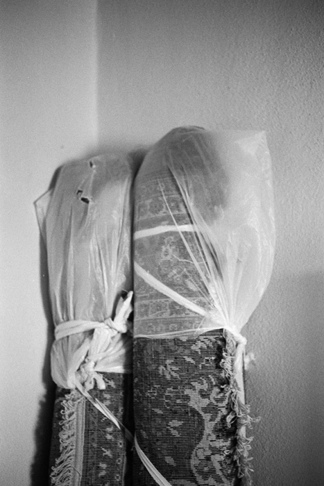 Two rolled-up rugs wrapped in plastic leaning against a wall.
