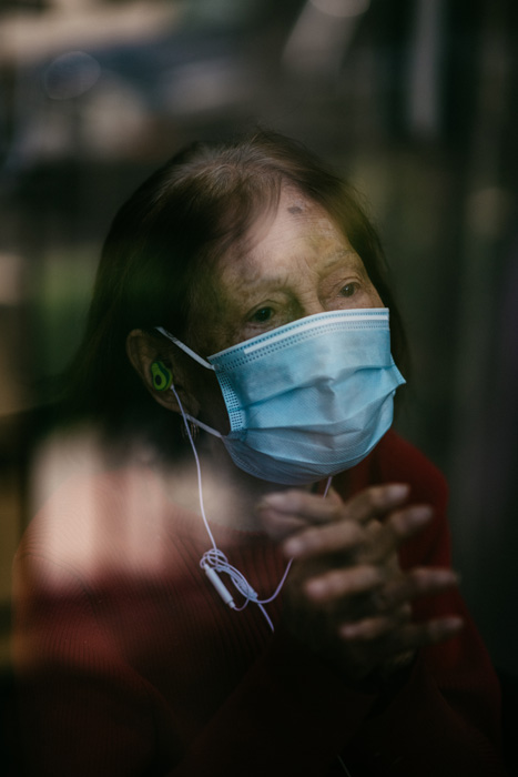A senior woman with a mask on, looking through a glass barrier.