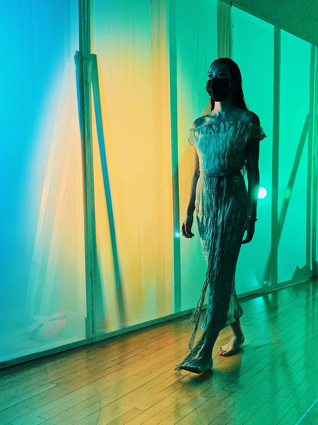 A model wearing a gauzy dress by a wall lit up in green and yellow.