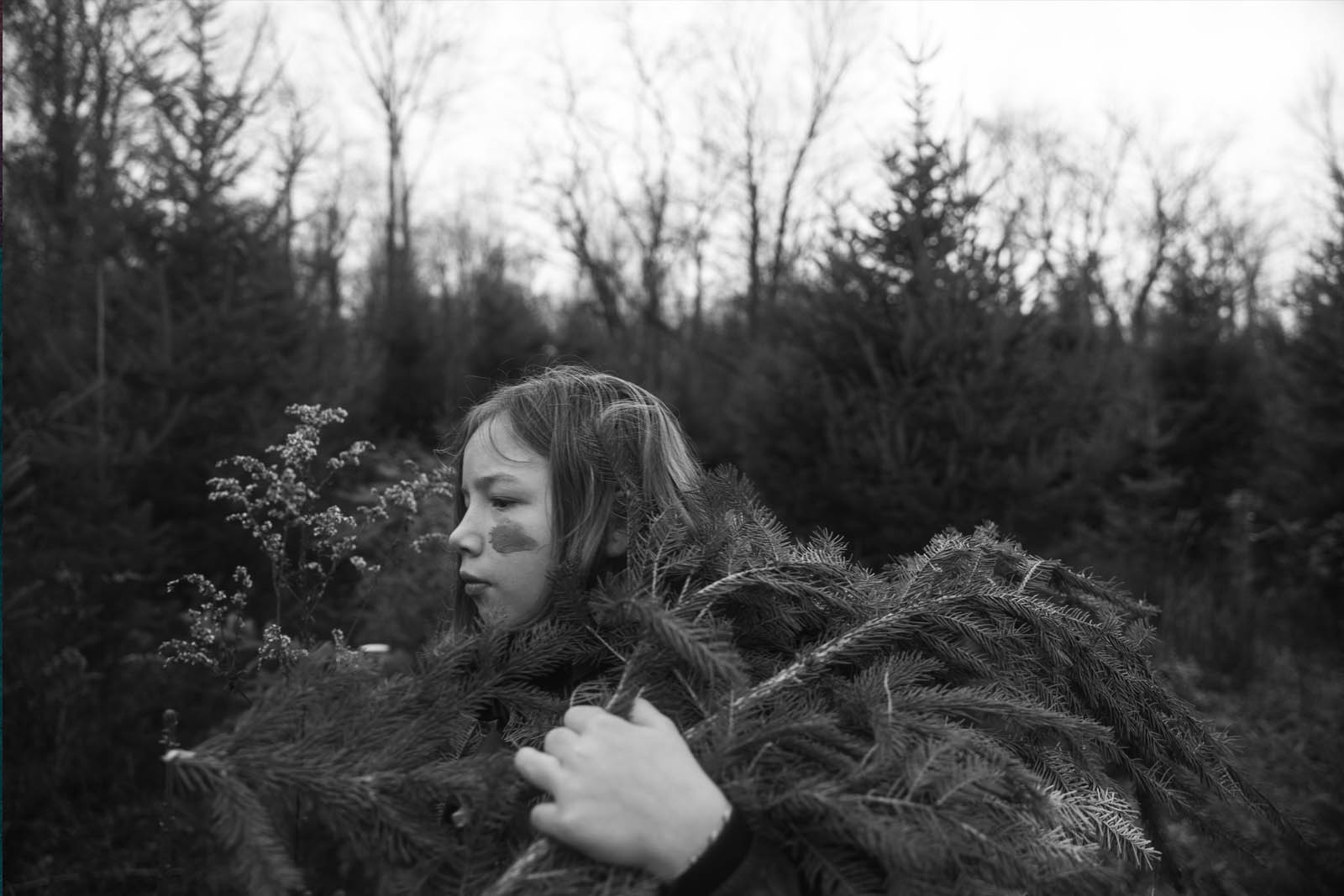 A young girl carrying tree branches in a black and white photo