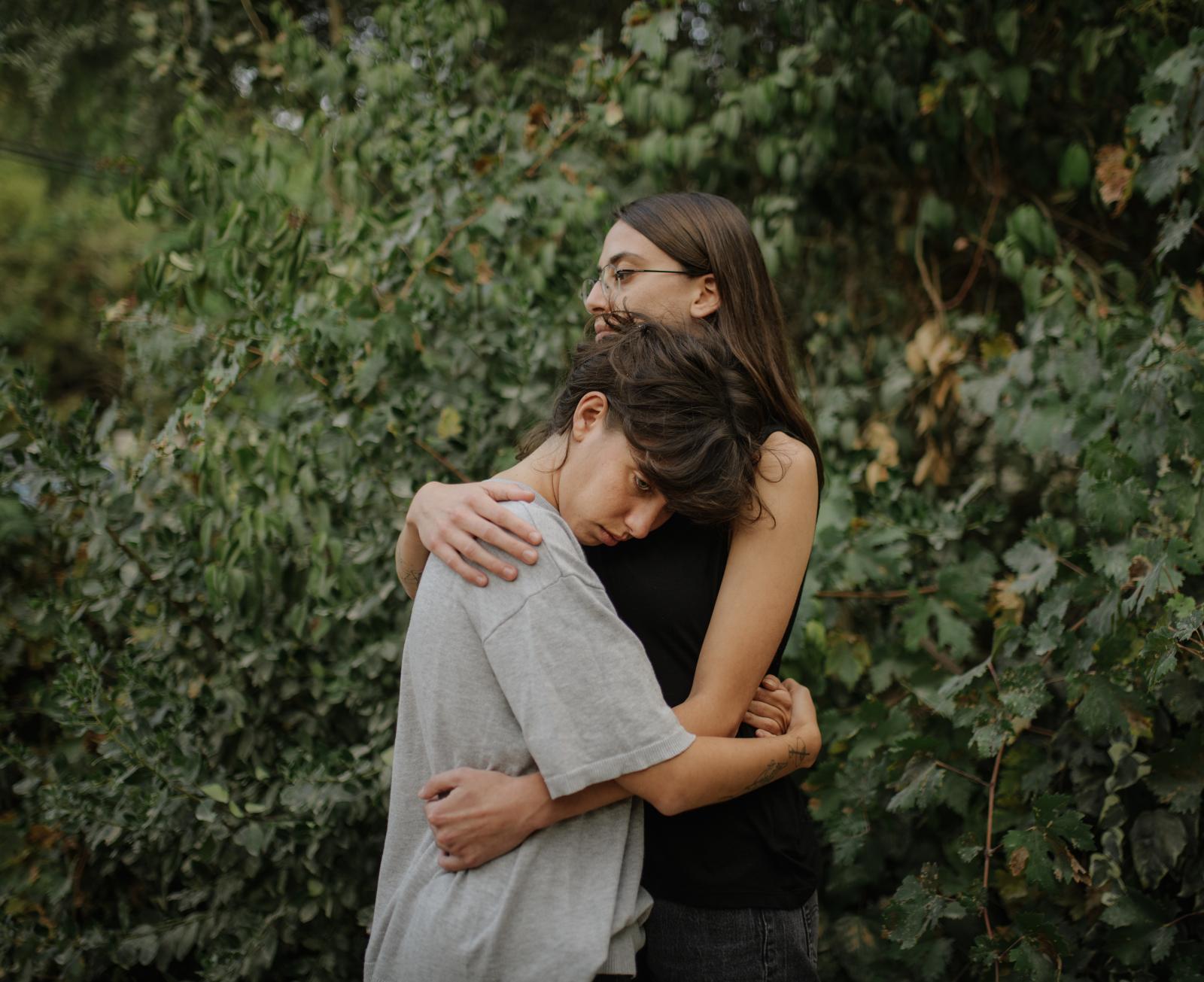 Shiri Furst, 24,(F) and Yael Dan, 24, (B), childhood friends, embrace in front of green foliage 