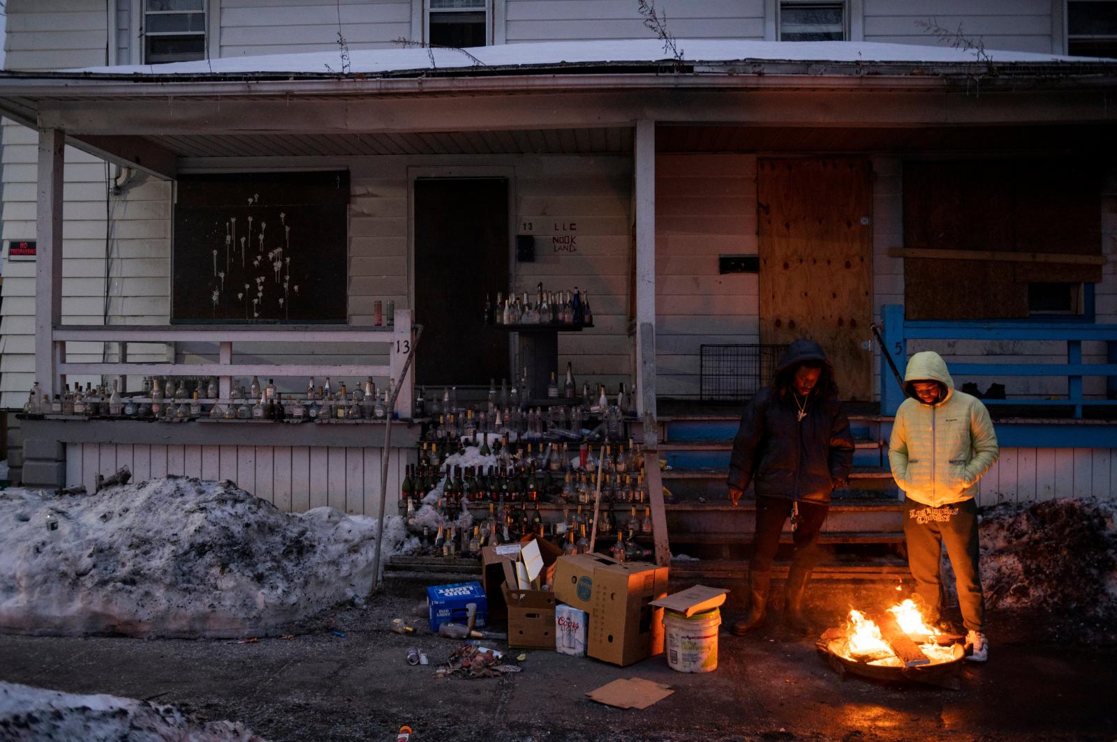 two people stand in front of a fire in front of a dilapidated house 