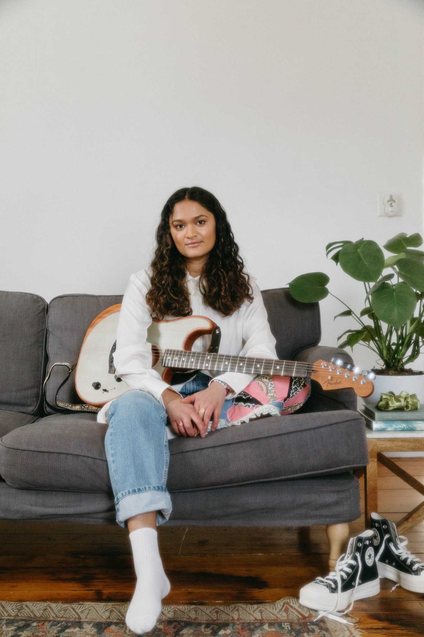 Padma Mynampaty sits on a couch holding a guitar